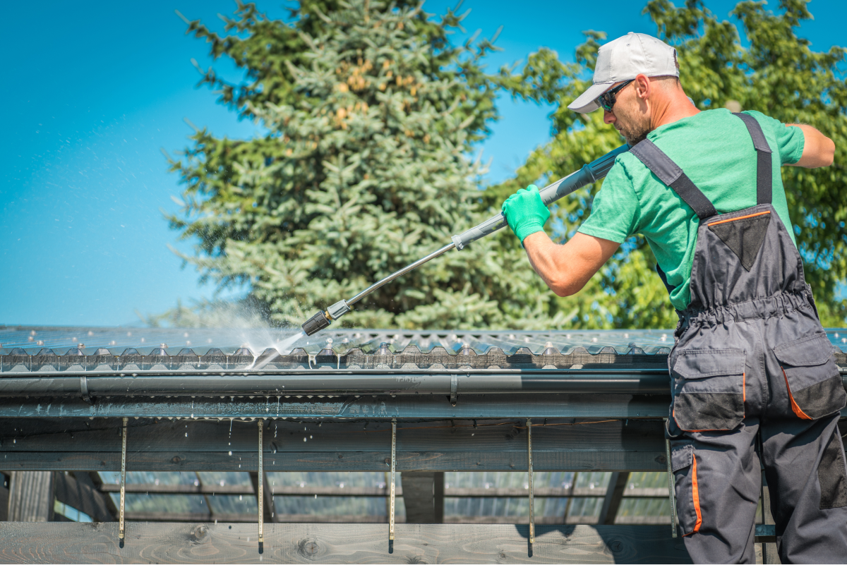 someone standing on a ladder cleaning the gutters of a house with a pressure hose