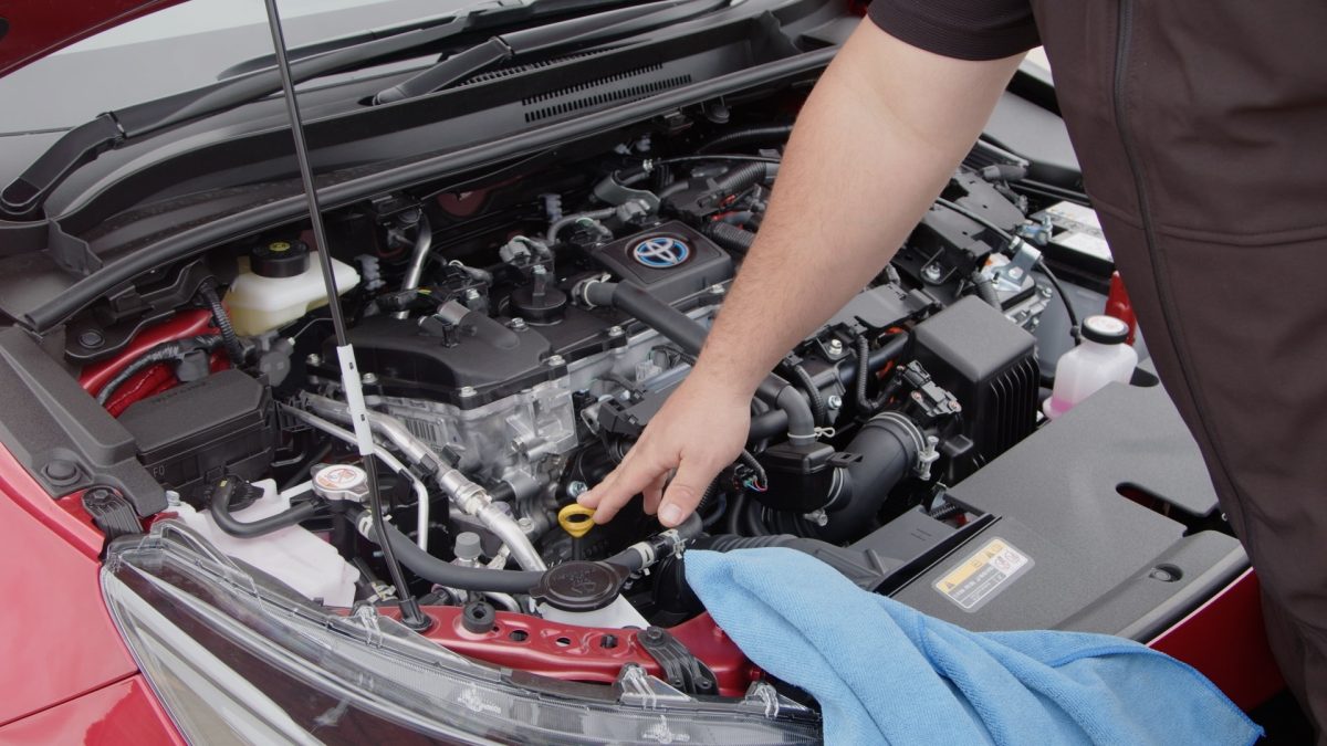 hand pointing to the yellow handle of the oil in a car