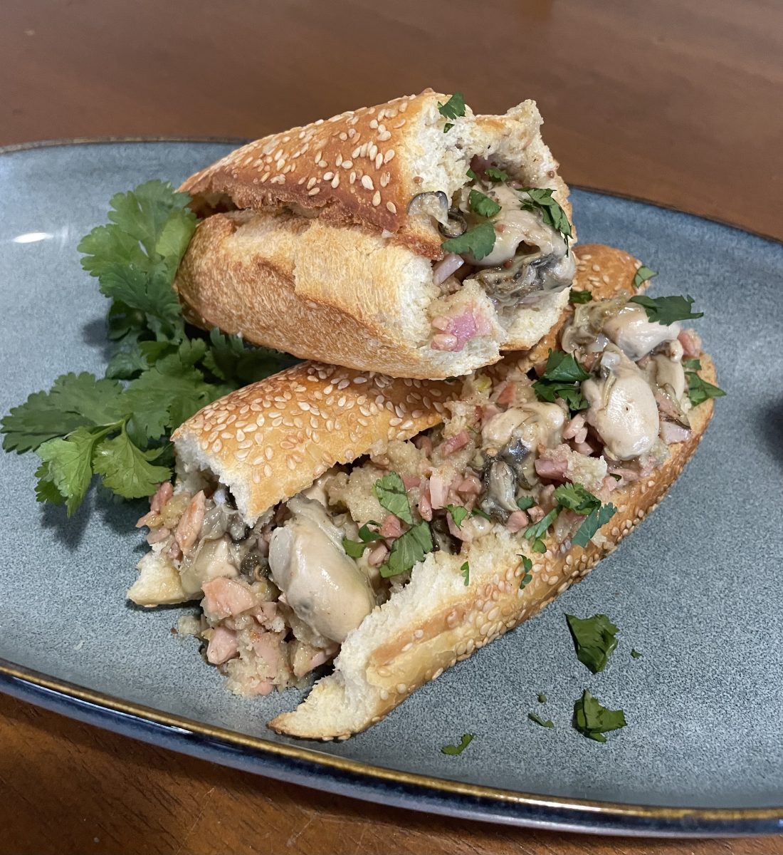 A plate with two Po Boy sandwiches stacked on top of each other, with oysters and bacon inside it.