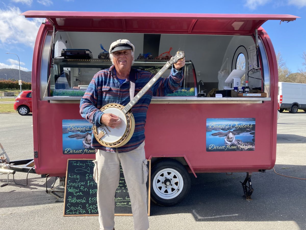 Banjo holding his banjo in front of the trailer he uses to sell oysters.