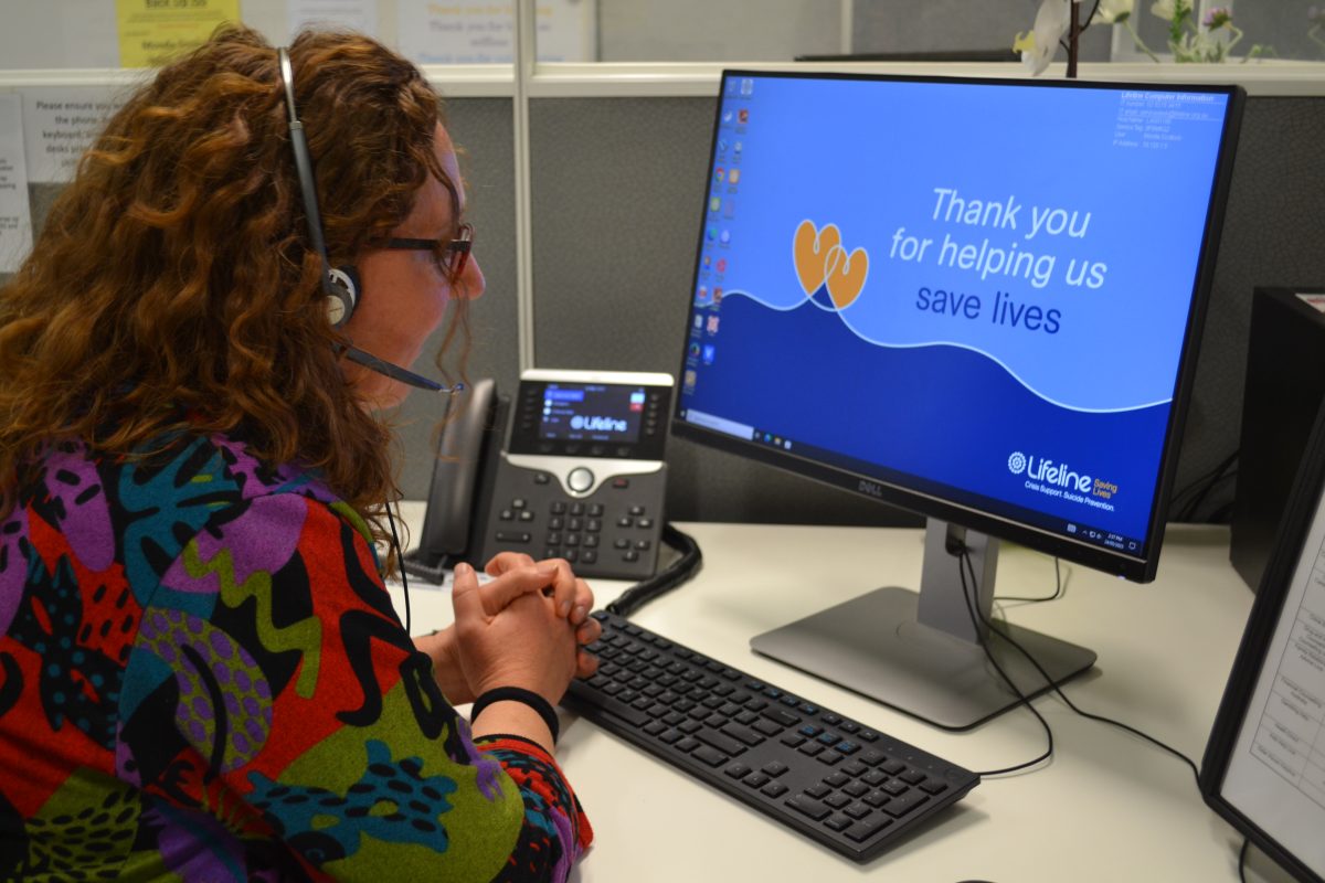 Lifeline crisis support worker wearing a headset and sitting in front of a computer that reads Thank you for helping us save lives