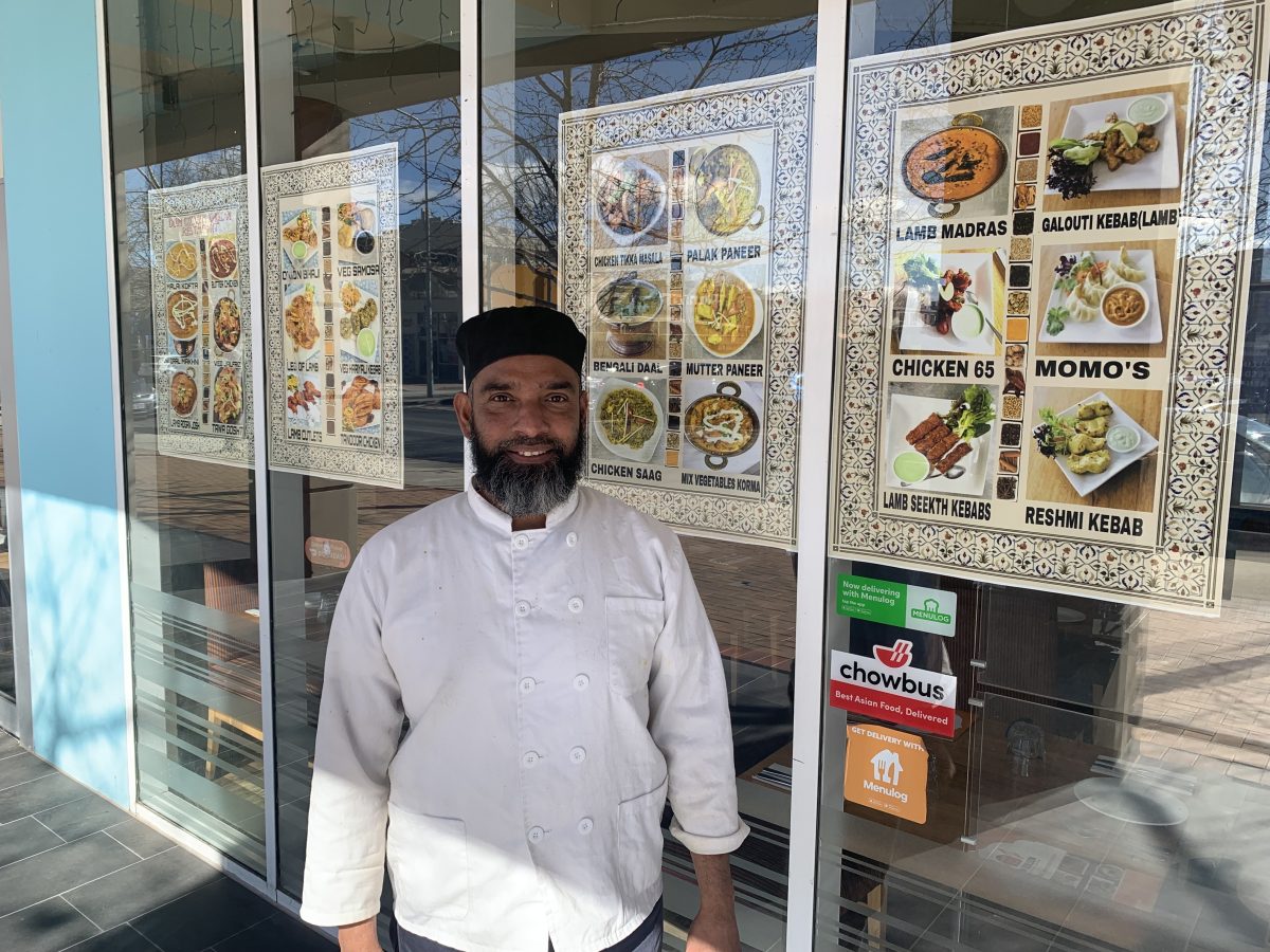 Adam standing out the front of his restaurant, with menu items behind the window.