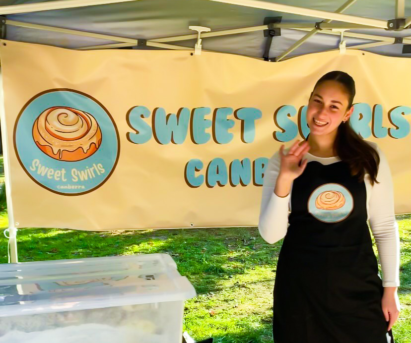 A teenager stands in front of branded Sweet Swirls banner and waves