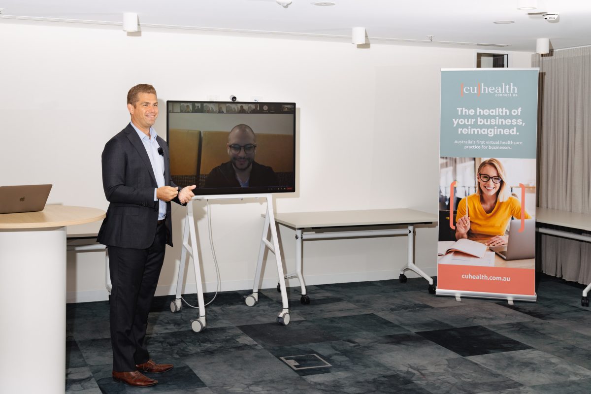 Man standing in front of a screen with virtual meeting and CU Health banner next to it