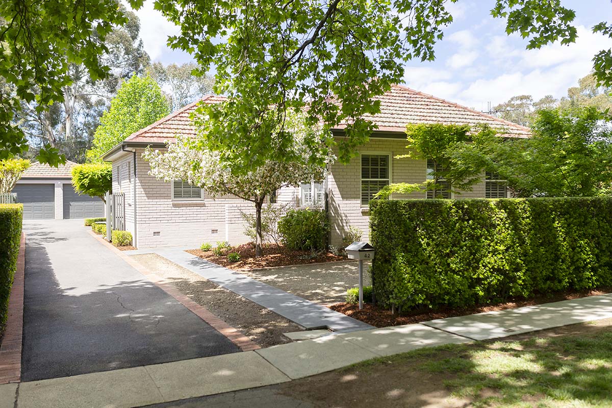 The front of the house with driveway on the left, hedge to the right, and a tree just before the stairs entering the home.