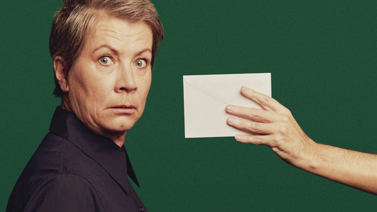 A short-haired older woman looking shocked with an envelope presented to her face, on a green background.