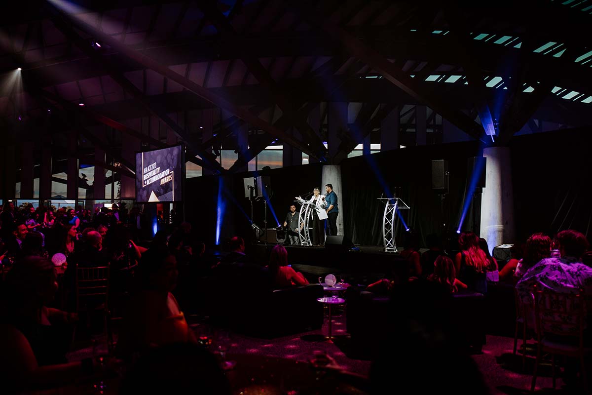 Function room at night full of people, with someone speaking at a podium.