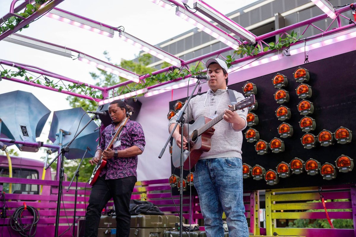 Two musicians playing guitar and singing on the back of a purple truck, which has been remodelled as a stage.