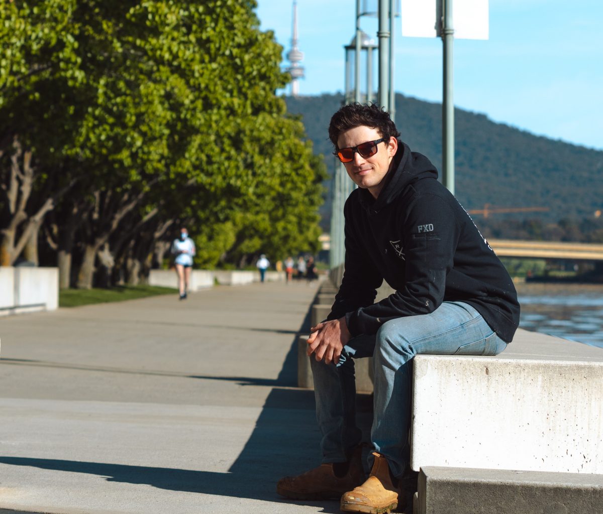 Connor sitting on a bench next to the shore of Lake Burley Griffin with the Telstra tower in the background.