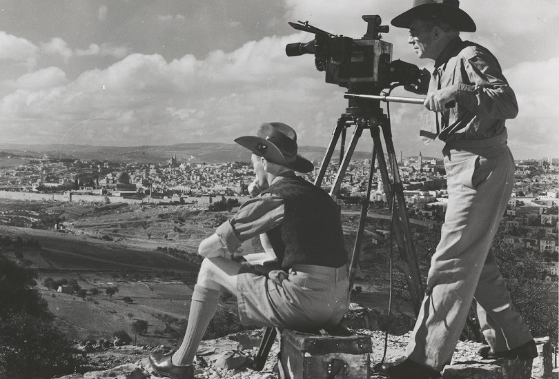 Two people with a large camera on a tripod looking over a cliff.