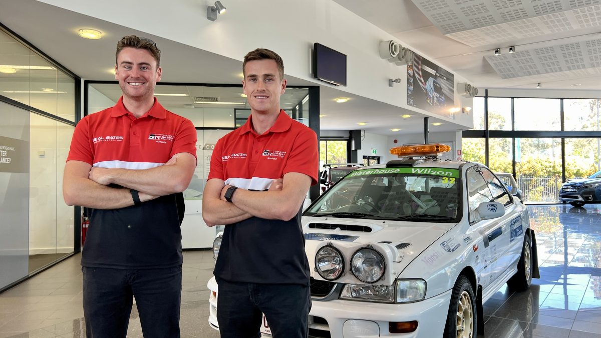 two men stading in front of a rally vehiucle in a car showroom