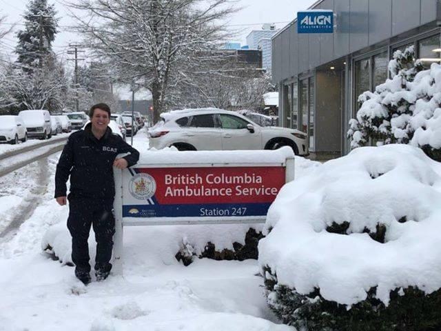 Richard standing in the snow next to a sign outside a building reading: "British Columbia Ambulance Service".