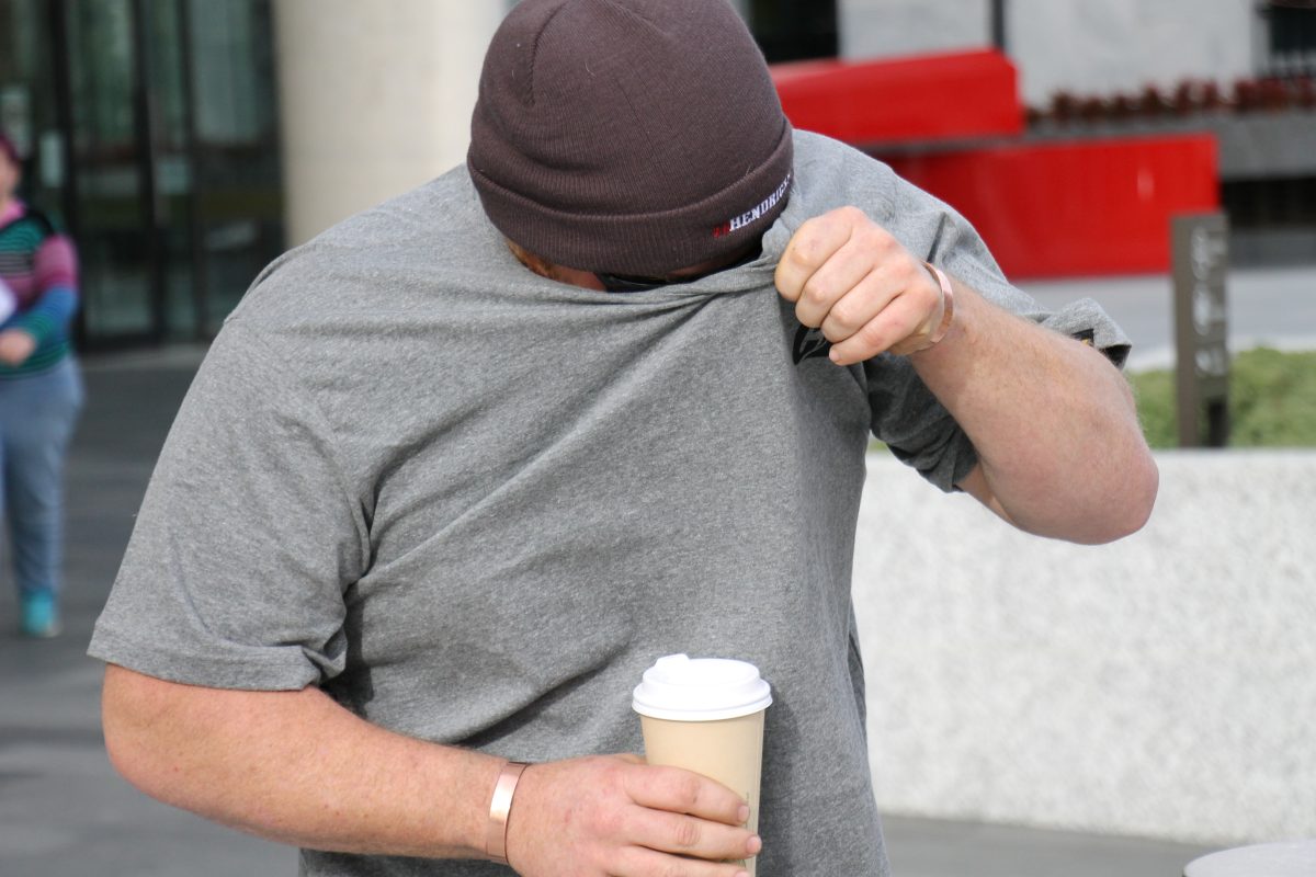man walks while holding a coffee and hiding his face from media