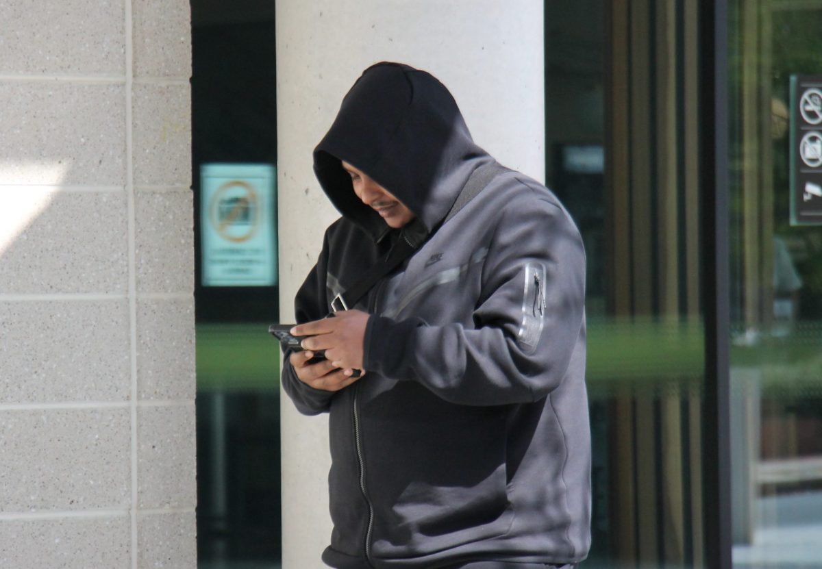 man in hoodies outside court reading his phone