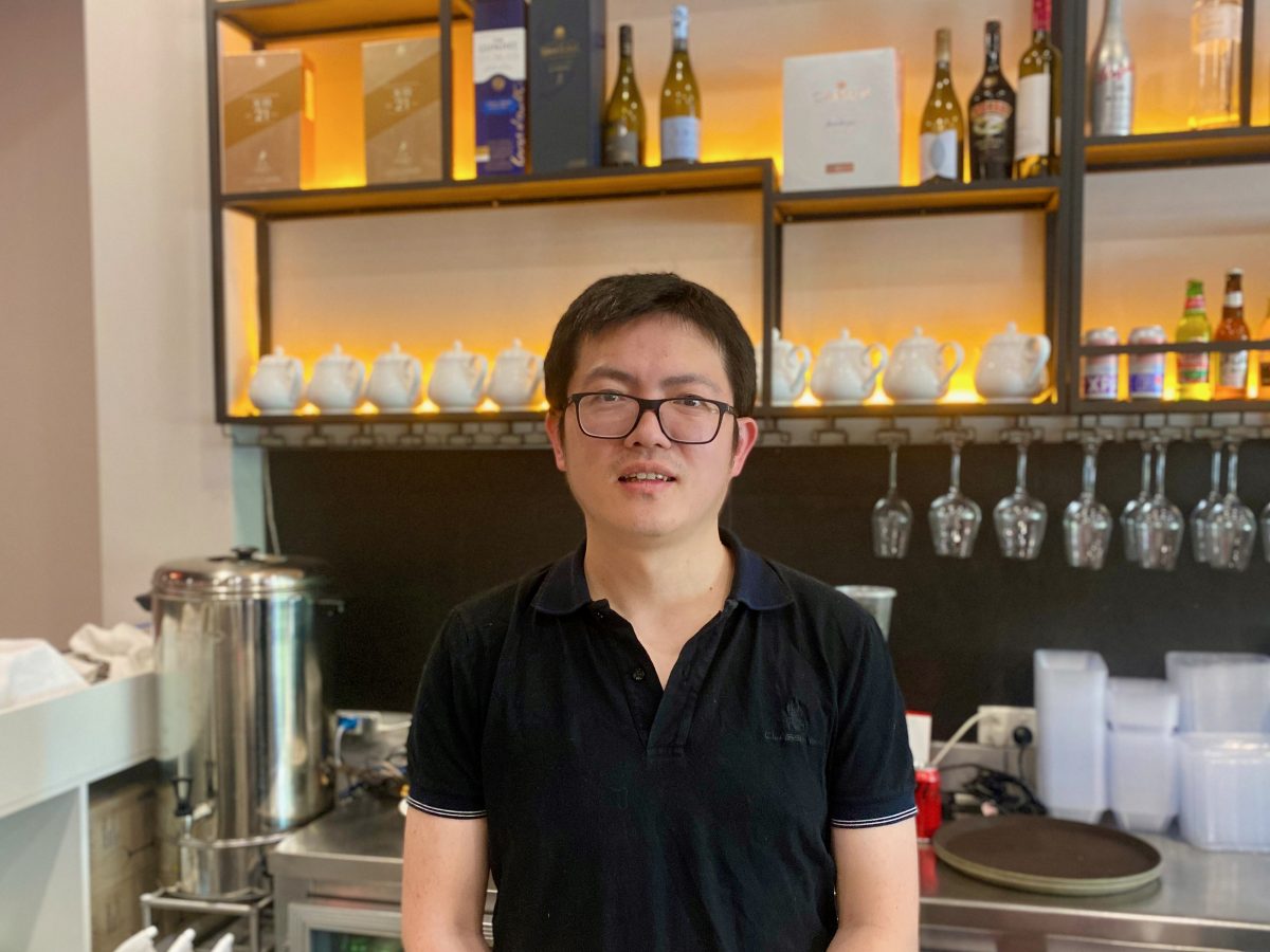 Man in glasses stands in front of bar counter with teapots in the background