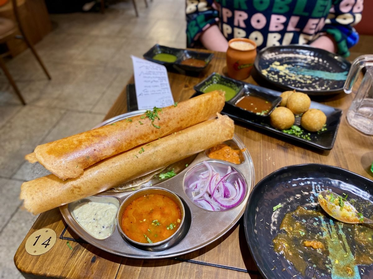 Silver tray with three rolled 'dosas' and different chutneys in small dishes.