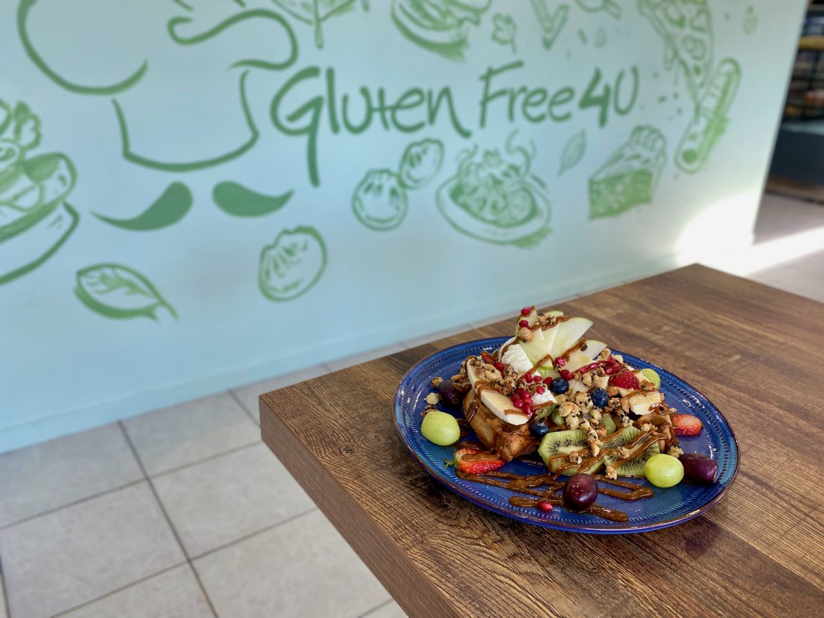 Colourful plate of waffles with fruit, in the background a mural reading Gluten Free 4 U