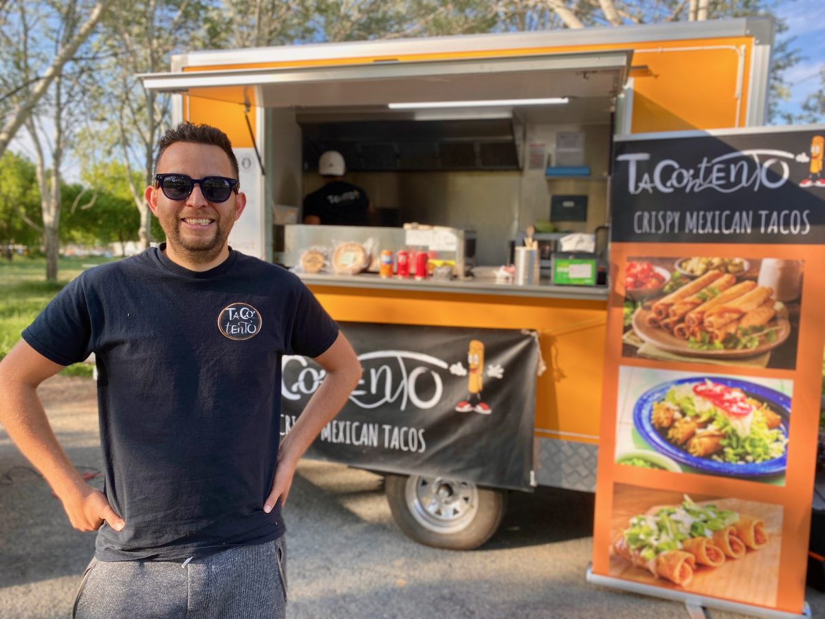 Alex stands with hands on hips in front of a yellow food van with a sign reading Tacontento with photos of food.