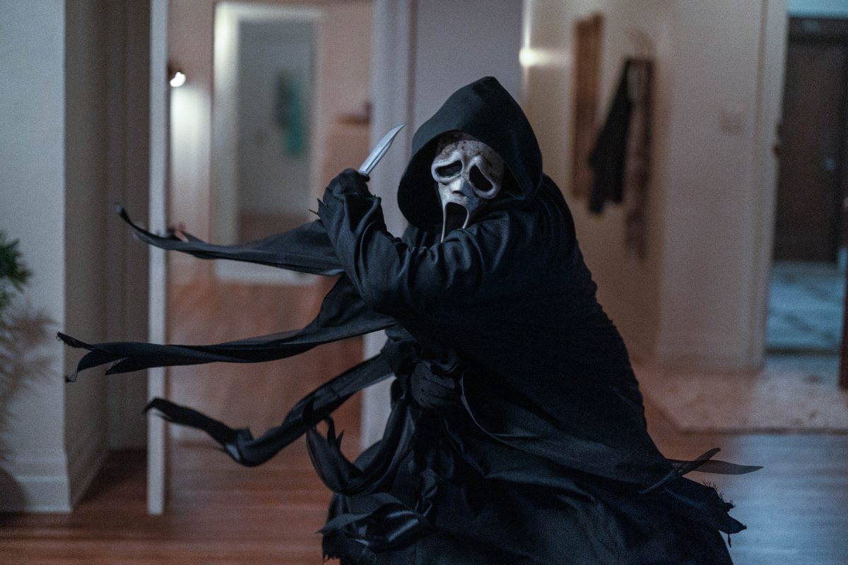 A screaming mask faced and hooded individual about to swing with a knife in a home. 