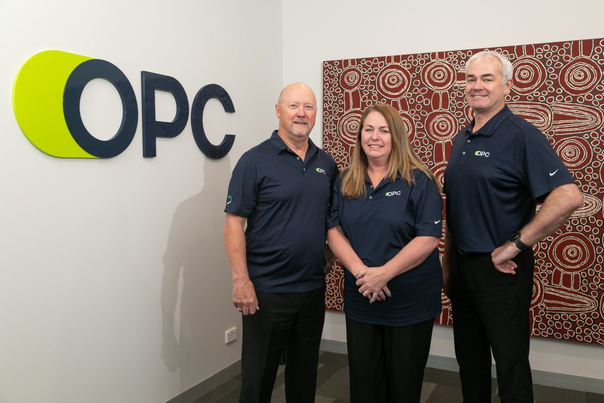 three people wearing OPC IT uniform standing in front of the OPC IT logo and a large artwork