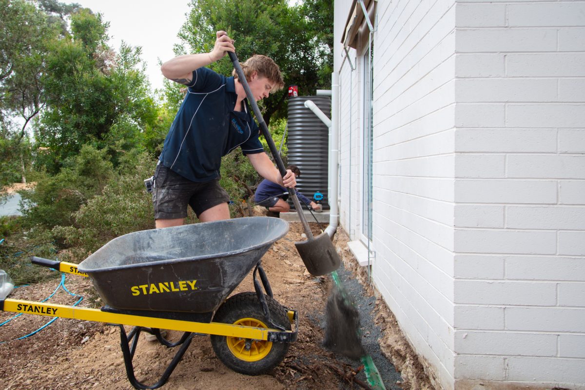 Blueline Plumbing & Gas installation employee digging beside wheelbarrow 