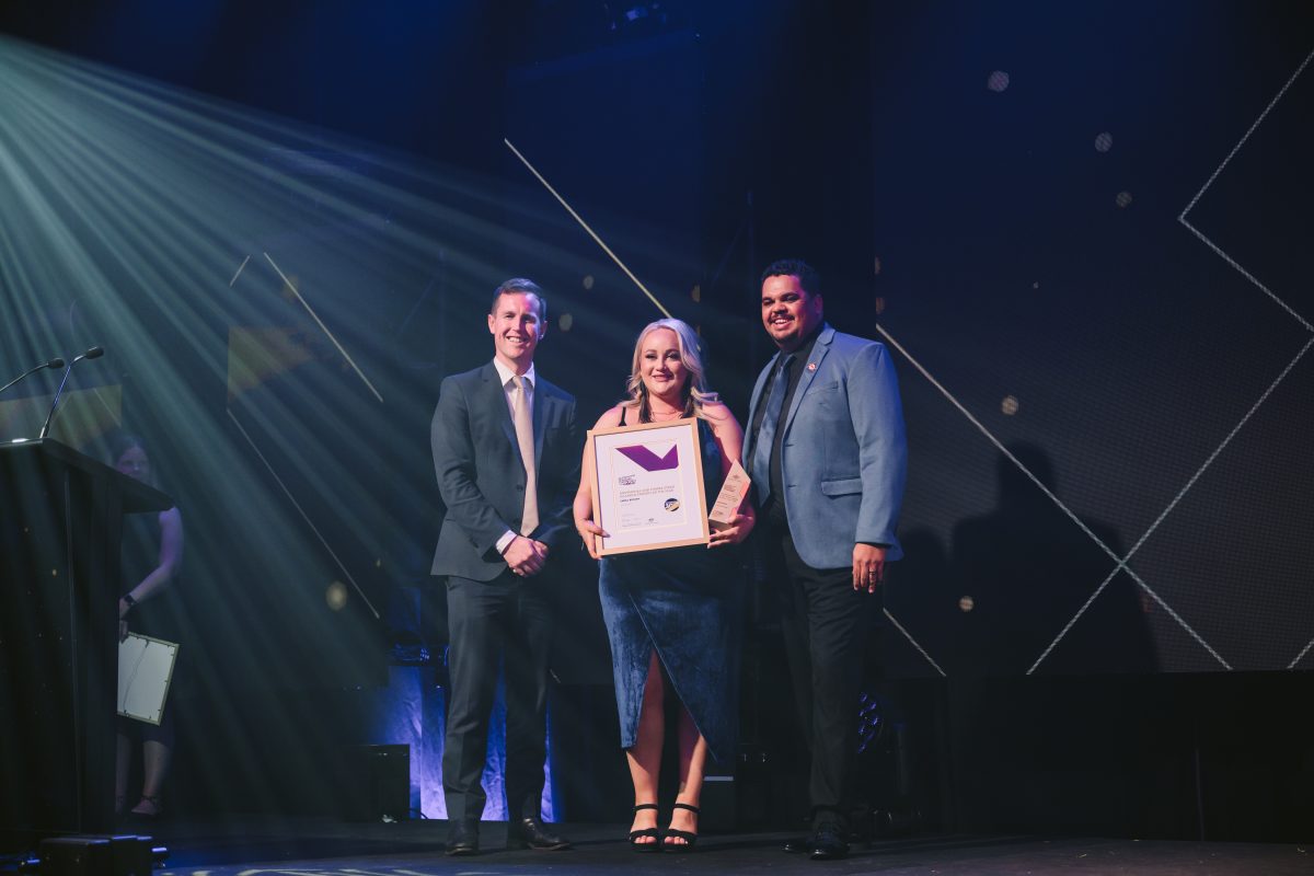 Emma Brown receives her award on stage with Chris Steel and Wayne Rider.