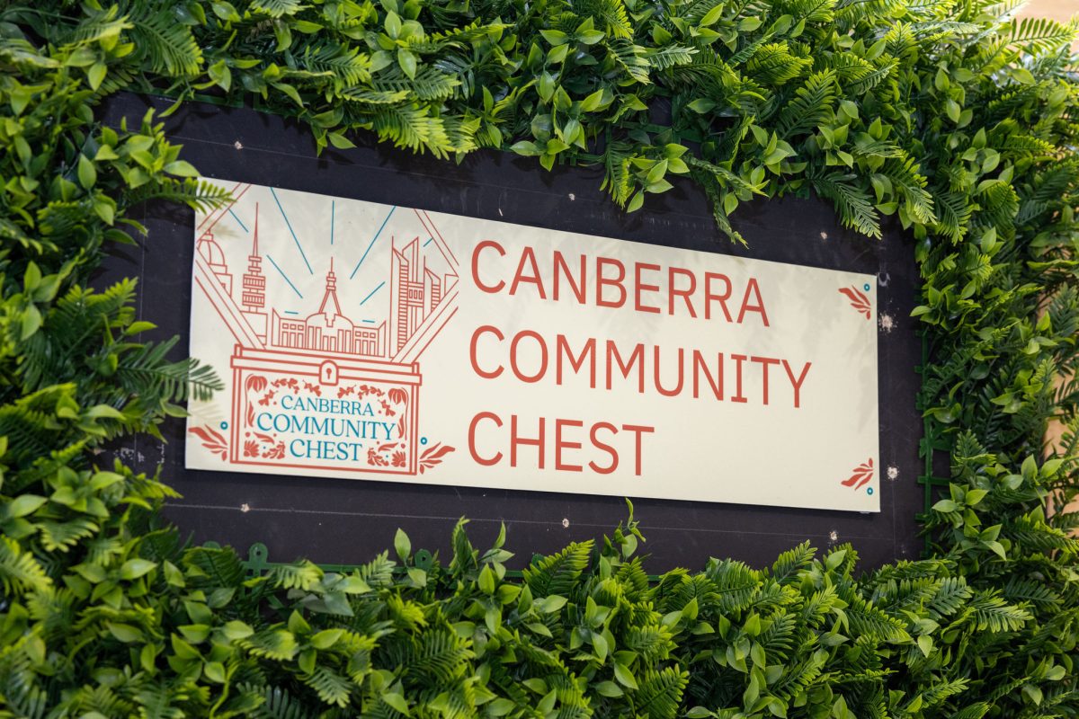 A sign reading "Canberra Community Chest" is framed by a hedge.