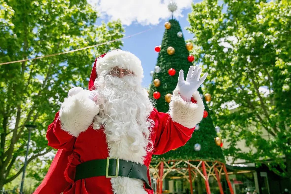 A man in a Santa costume in front of a fake Christmas tree