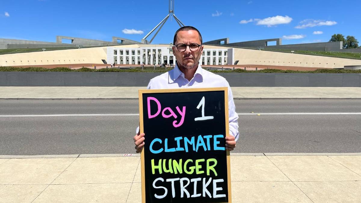 Gregory Andrews holding a sign stating 'Day 1 Climate Hunger Strike' while standing in front of Parliament house.
