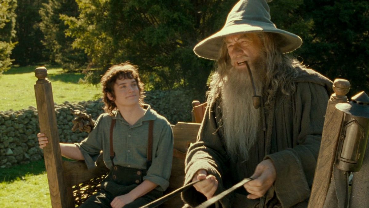Gandalf and Bilbo in a wooden carriage on a road in Hobbiton. 