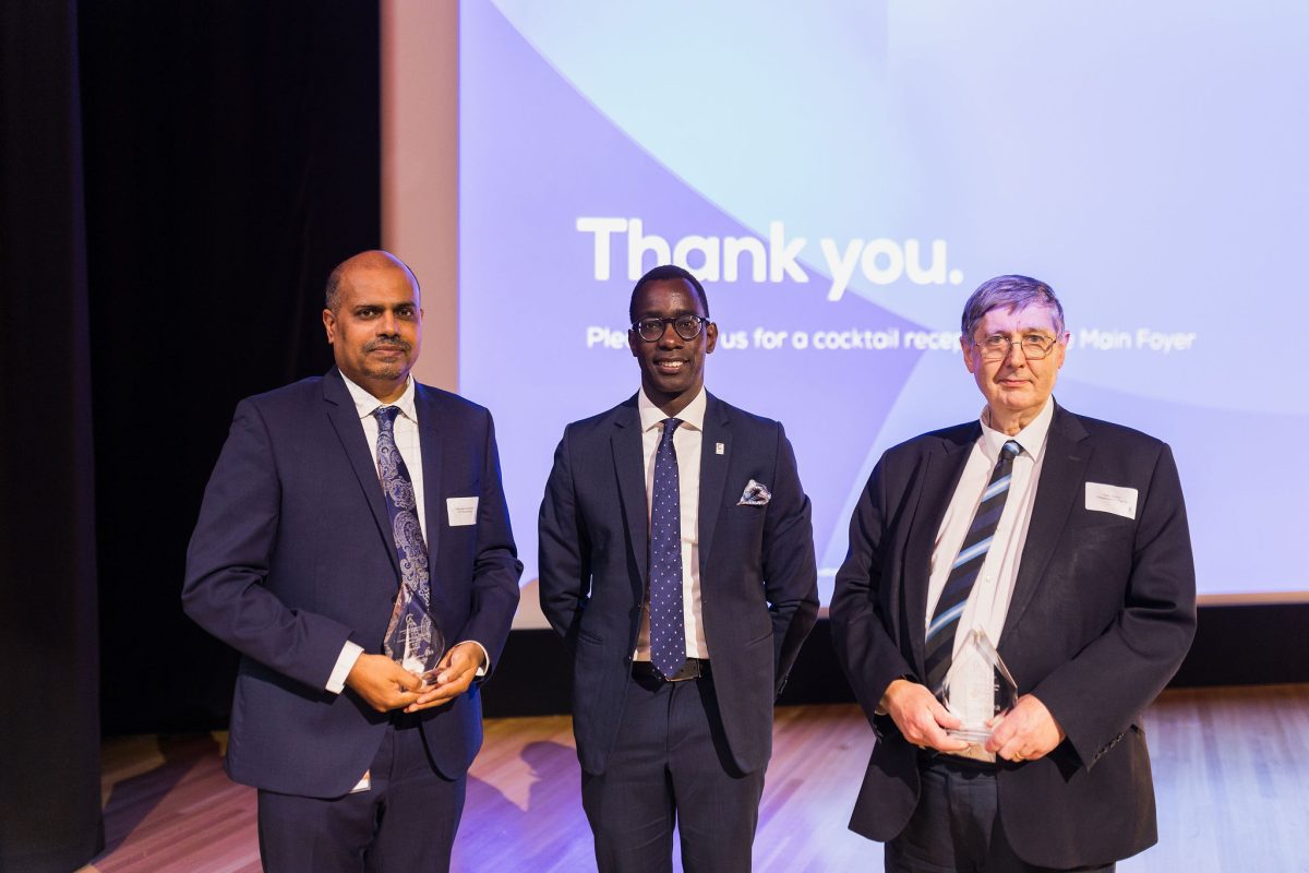 three men on stage with awards