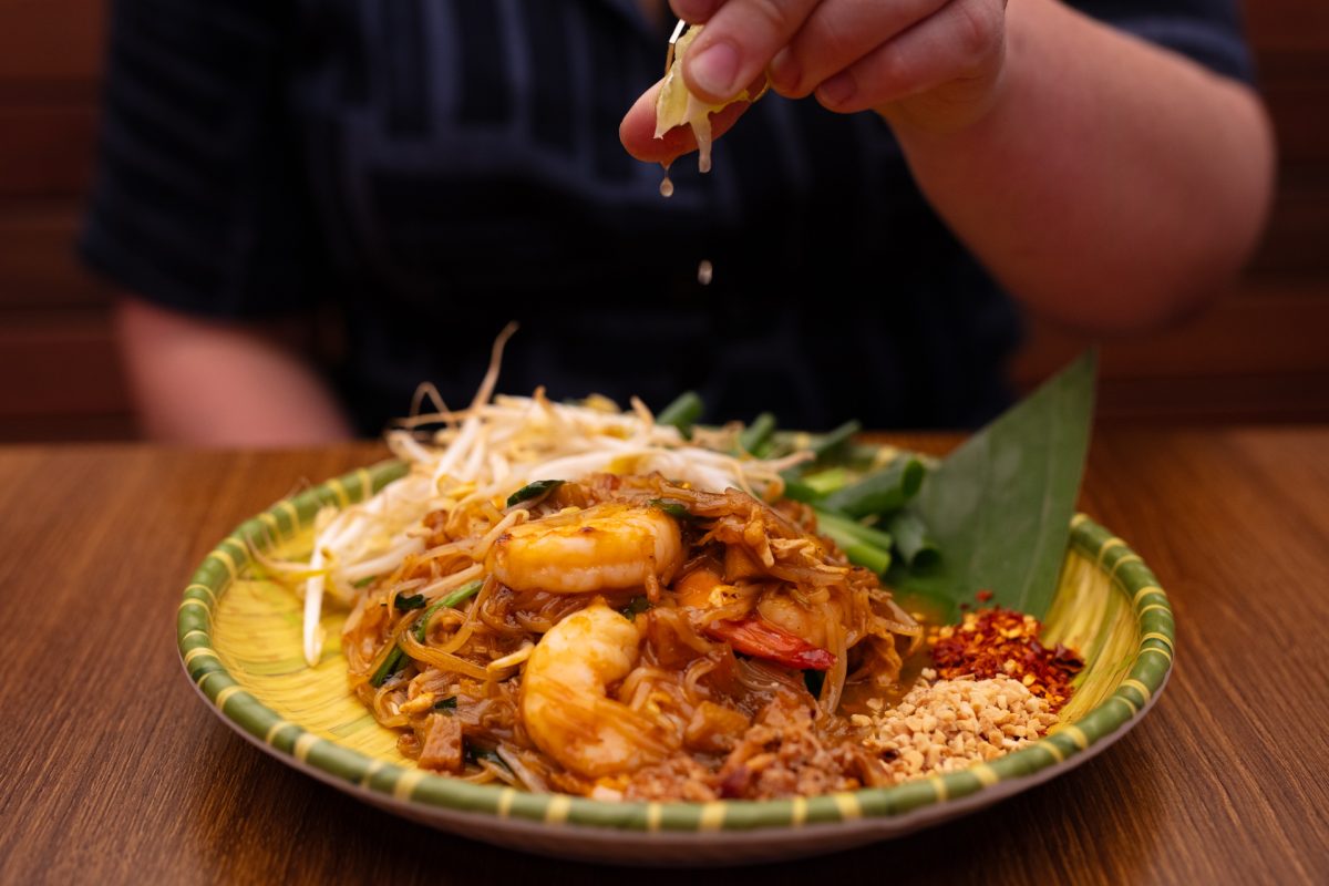 Hand squeezes lime onto plate of noodles.