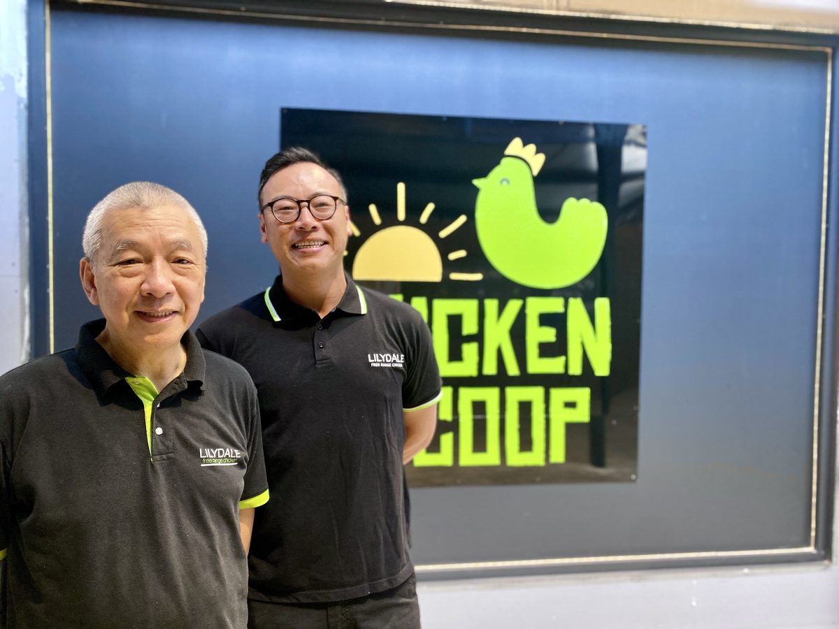 A father and son stand in front of Chicken Coop sign