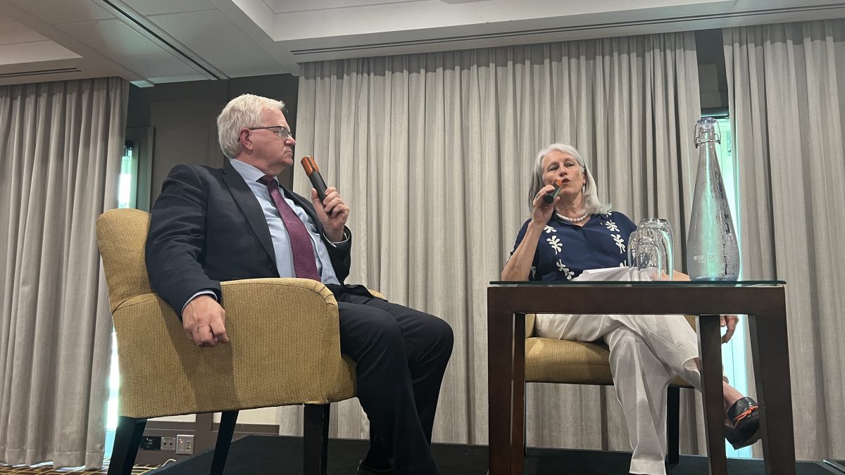 Professor Schmidt and Genevieve Jacobs talking to each other through microphones while seated. 