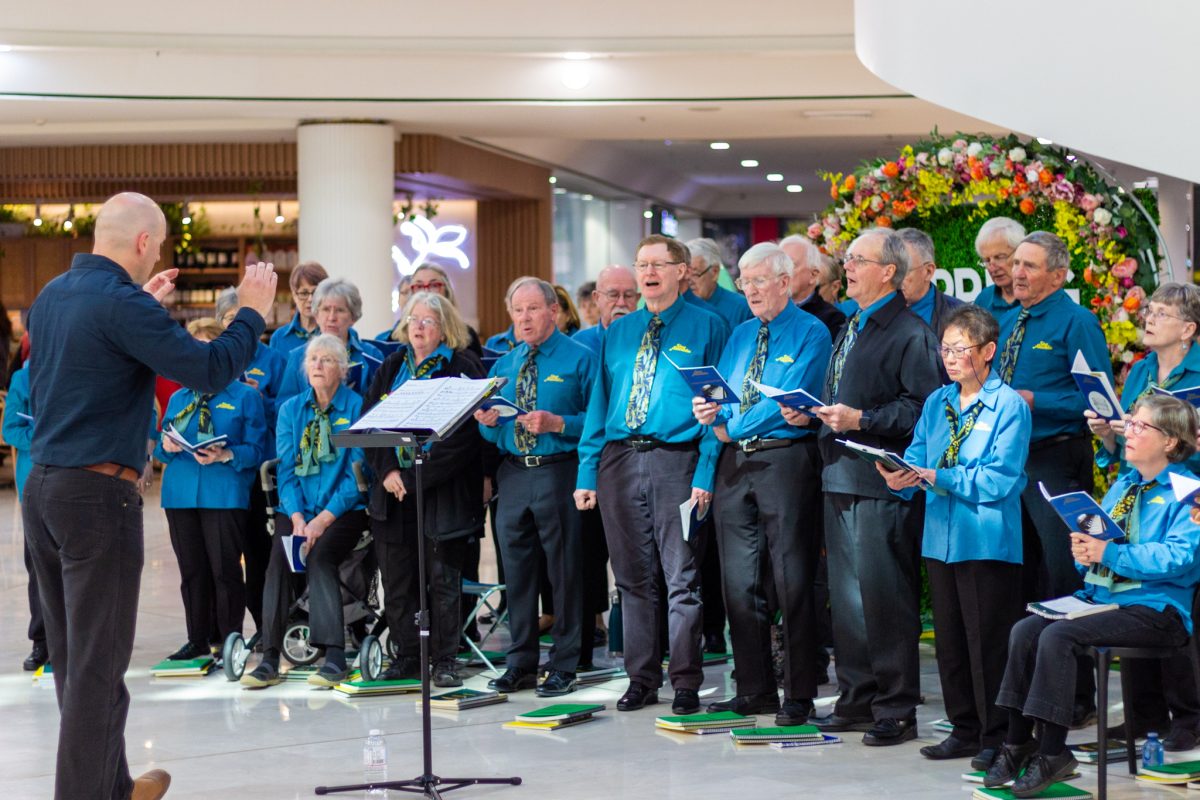 A group of people in blue shirts and black pants singing and a conductor