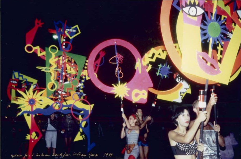 People at a float holding up brightly-coloured designed objects