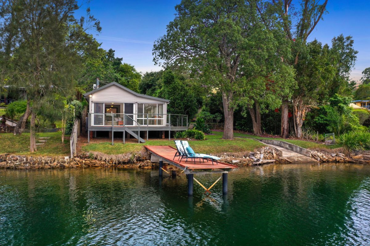 A house surrounded by threes with a jetty extending into a river