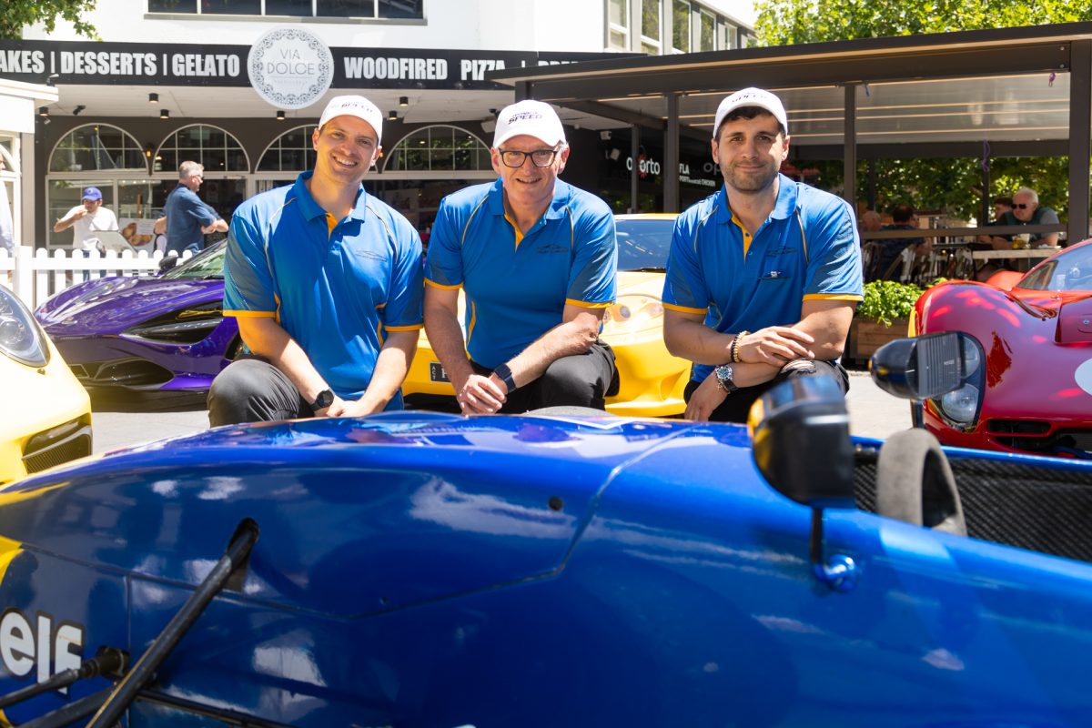 Three men crouching near sports car