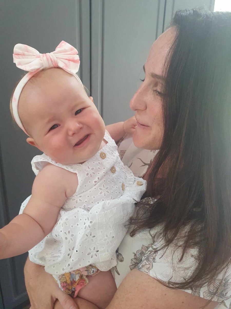 A woman with brown hair holds a baby in a pink bow. The baby is crying and the woman is trying to calm her down. 