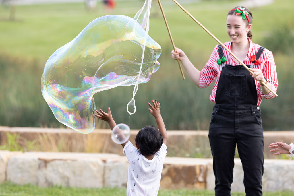 A woman making a large bubble and a child reaching for it