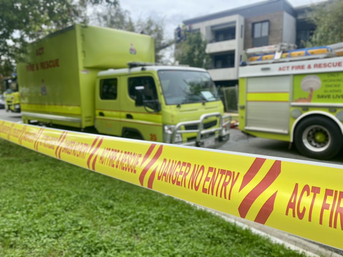 Yellow and red tape reading "ACT Fire and Rescue" and "danger no entry" in front of scene with yellow fire trucks.