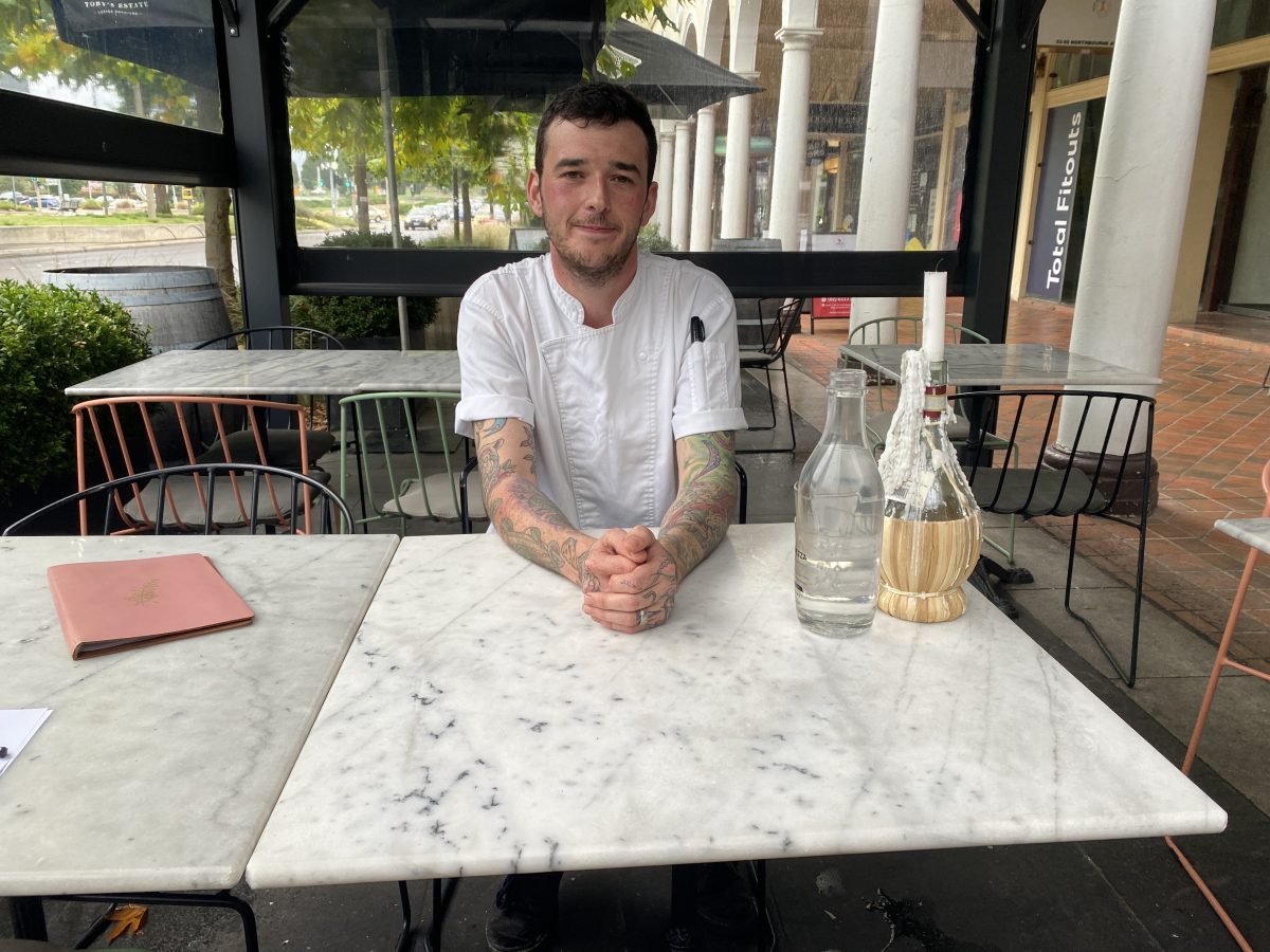 A White man with a short-sleeved shirt and tattoo sleeves sitting at a table