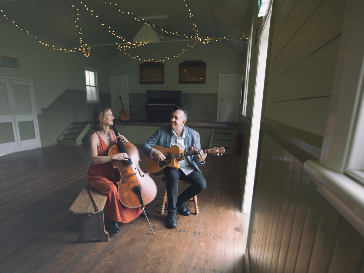 Cellist Ilse De Ziah and guitarist Ian Date in an empty hall with their instruments, looking at each other