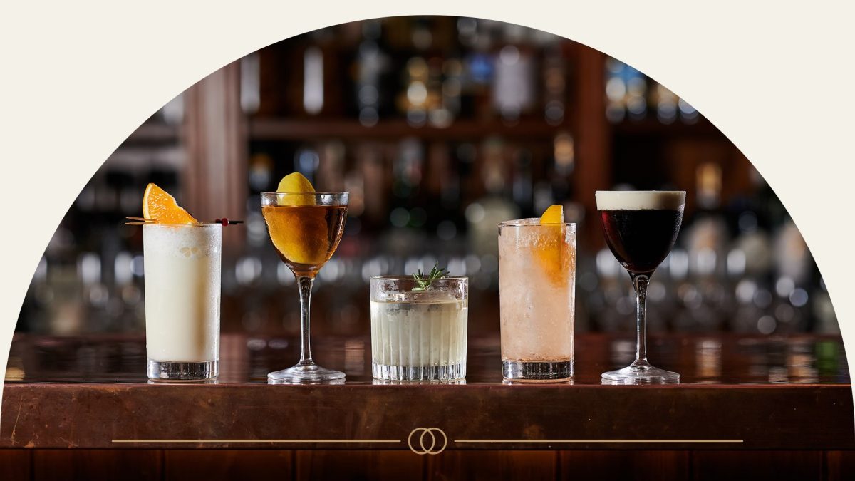 Five varying drinks in different glasses lined up on a bar counter