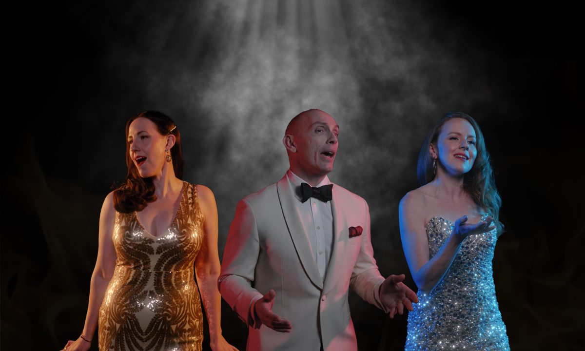 Two women and a man singing on stage wearing shiny clothes