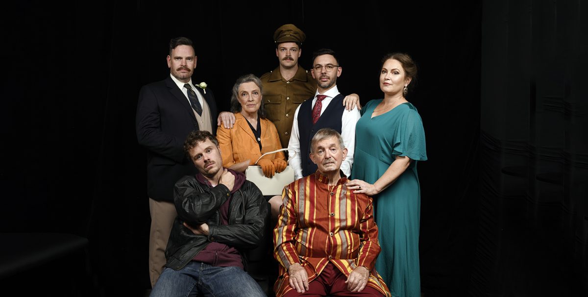 The costumed cast of the 2024 'Queers' production perched around a couch with a black background.