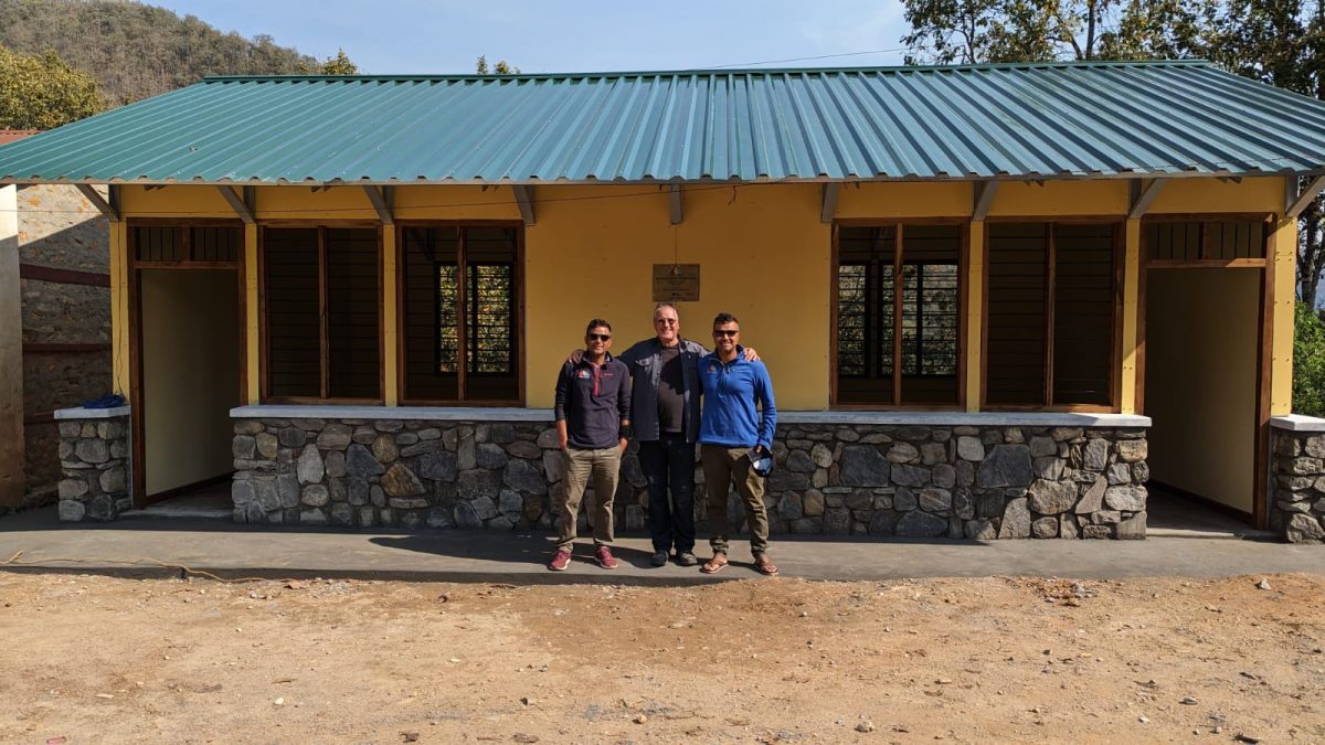 three people standing in front a newly built classroom in Nepal