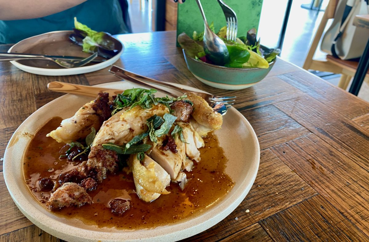 Plate of roast chicken with bowl of greens in background.