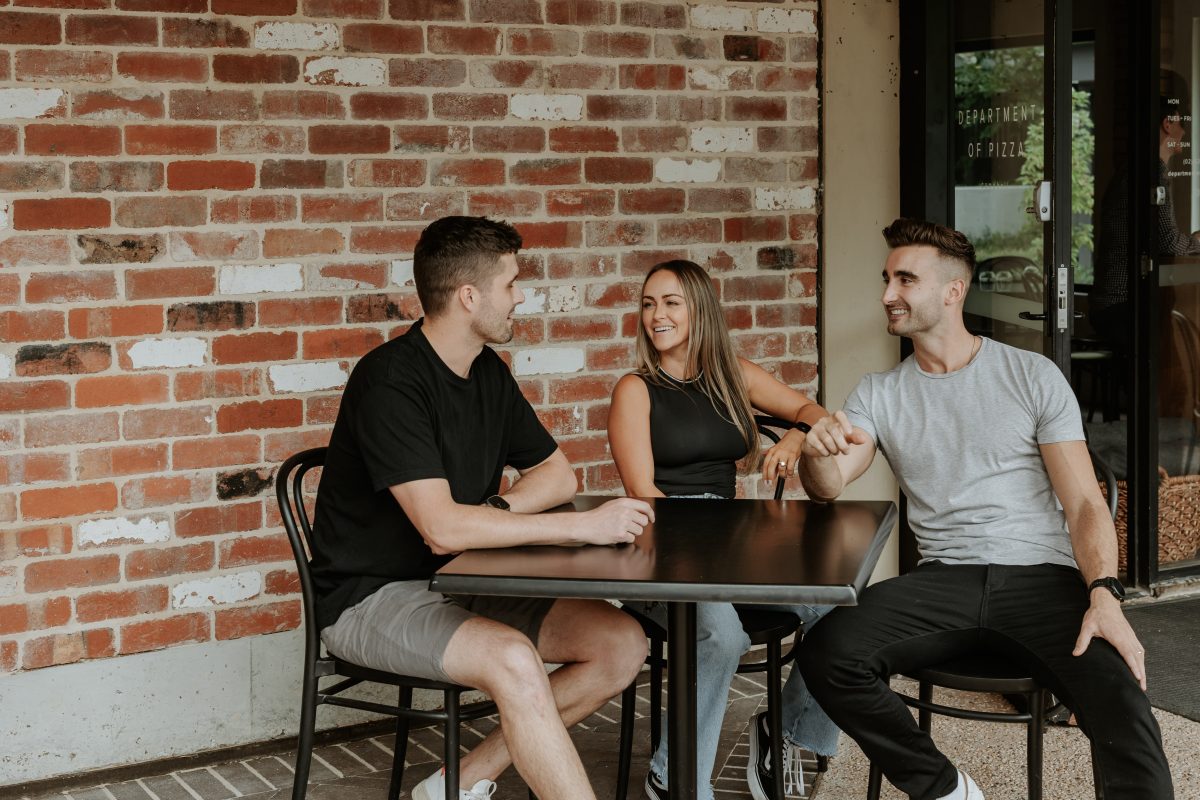 two men and woman sitting at table outside