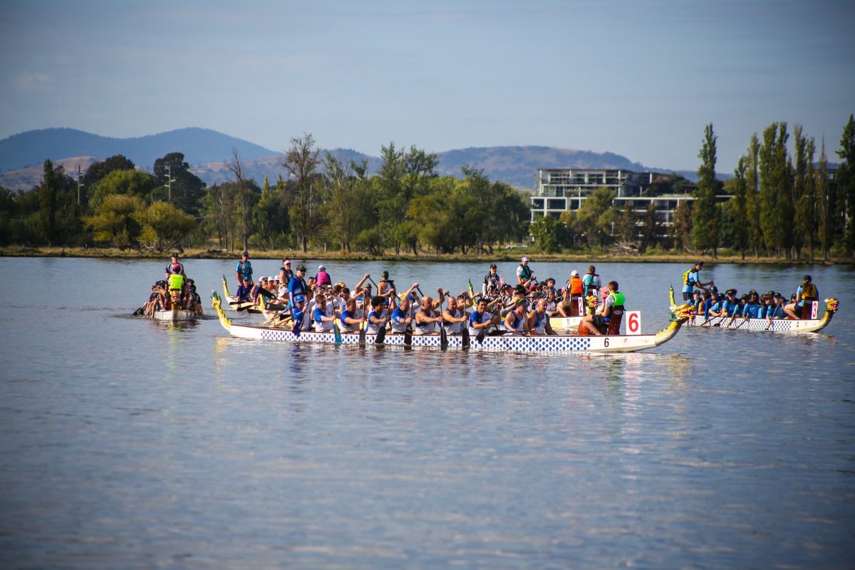 Three dragon boats on a lake, filled with people